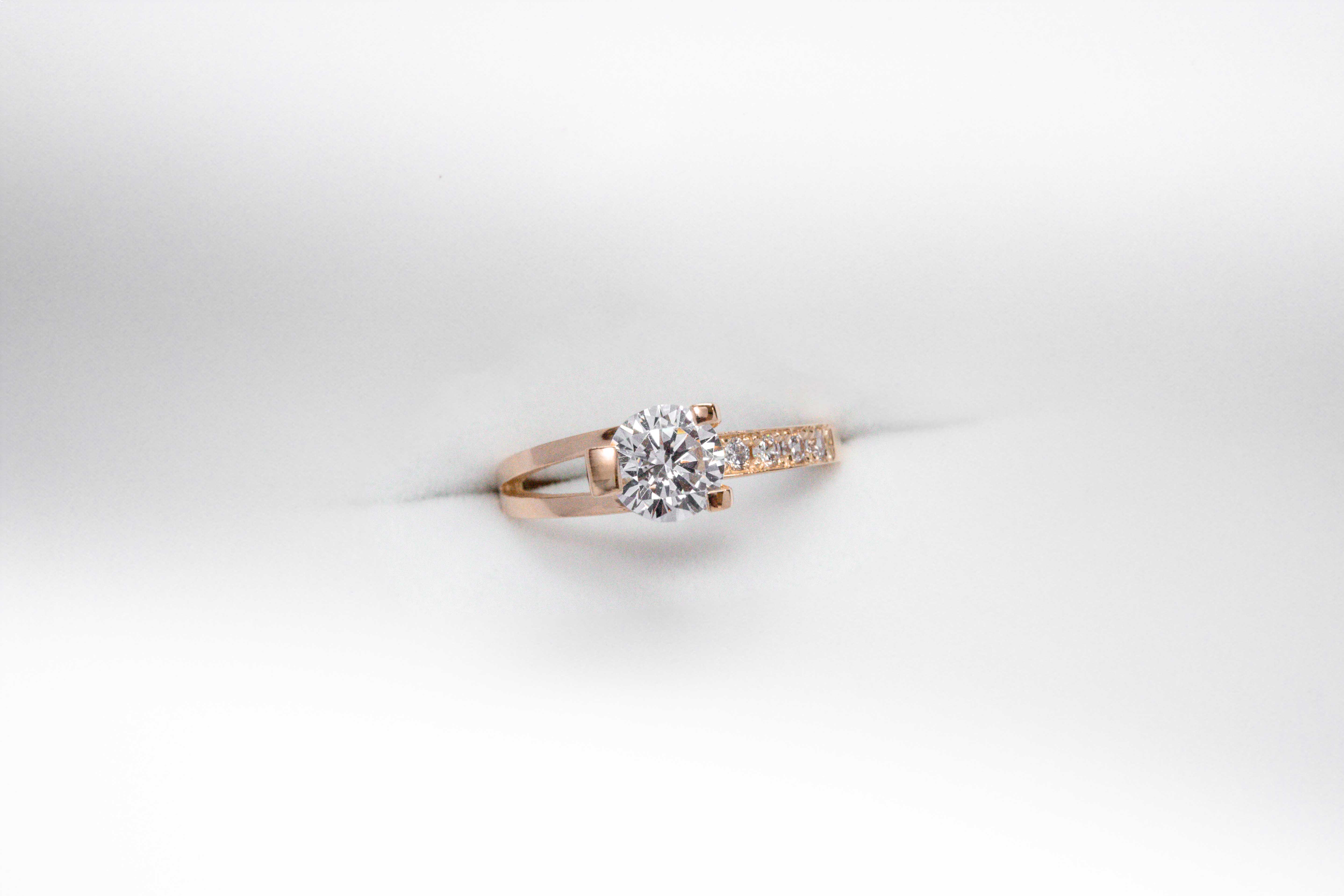 anillo de compromiso de oro 18k rosa con un diamante central y 4 diamantes mas pequeños en el costado sobre fondo blanco