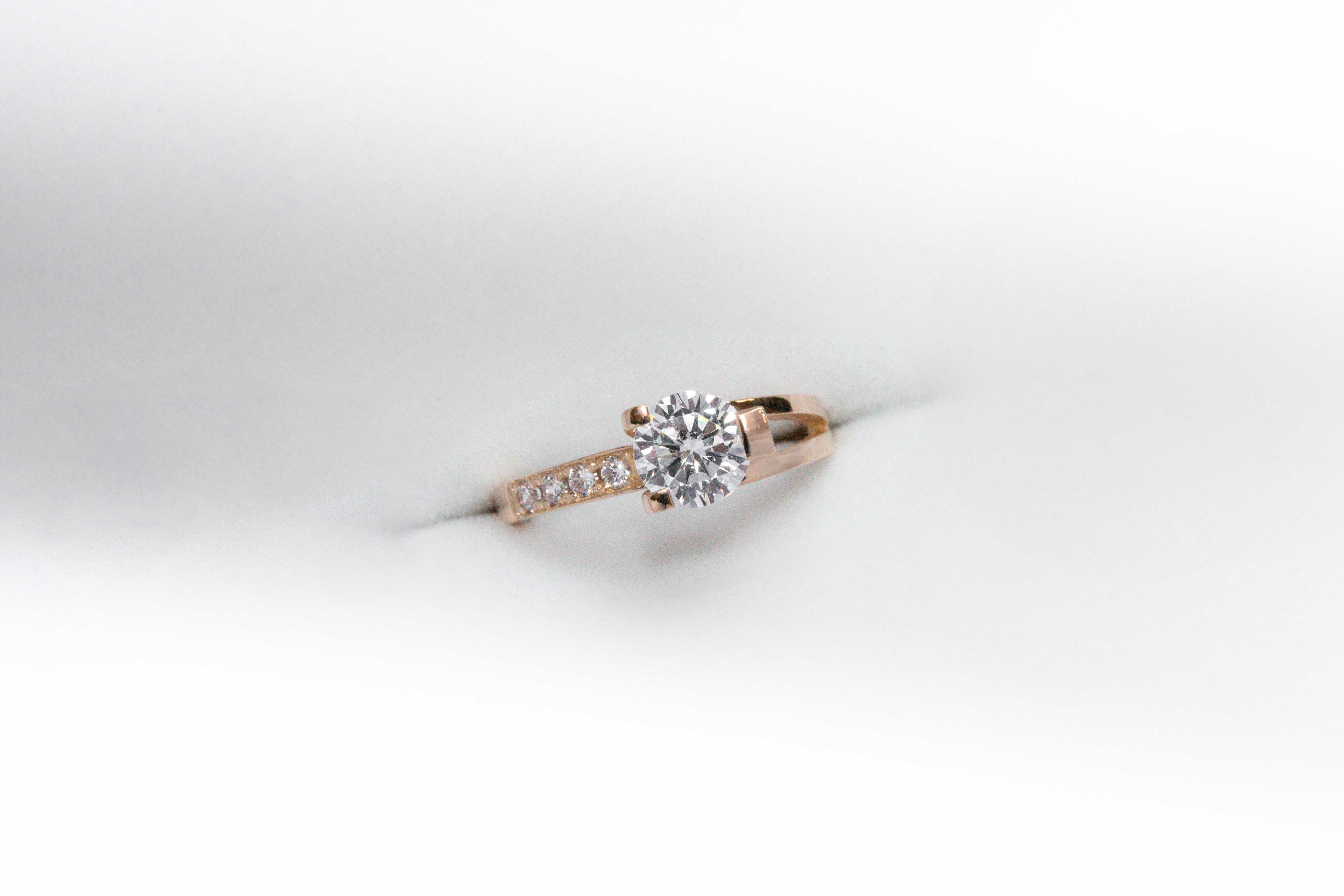 anillo de compromiso de oro 18k rosa con un diamante central y 4 diamantes mas pequeños en el costado sobre fondo blanco