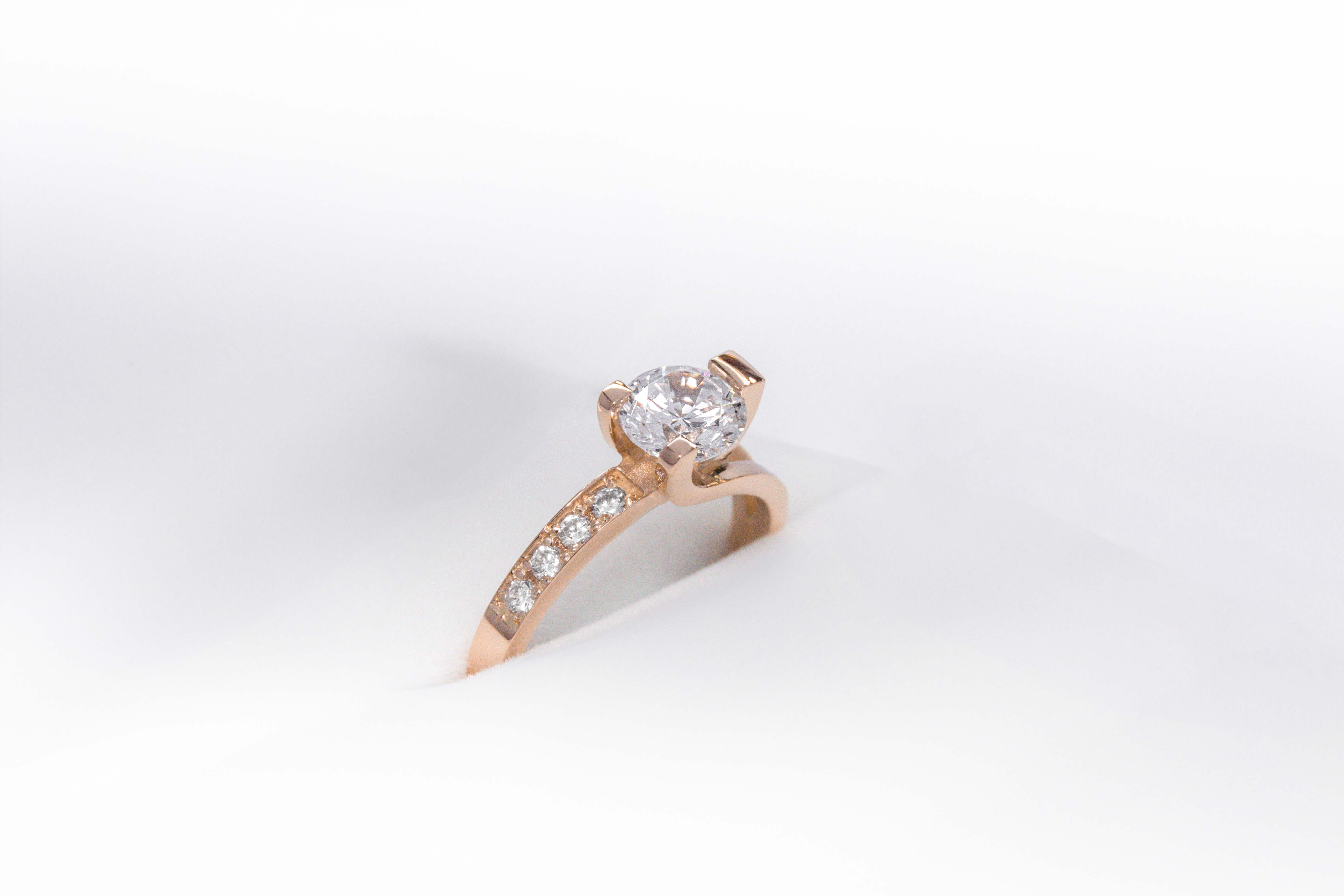 anillo de compromiso de oro 18k rosa con un diamante central y 4 diamantes mas pequeños en el costado sobre fondo blanco