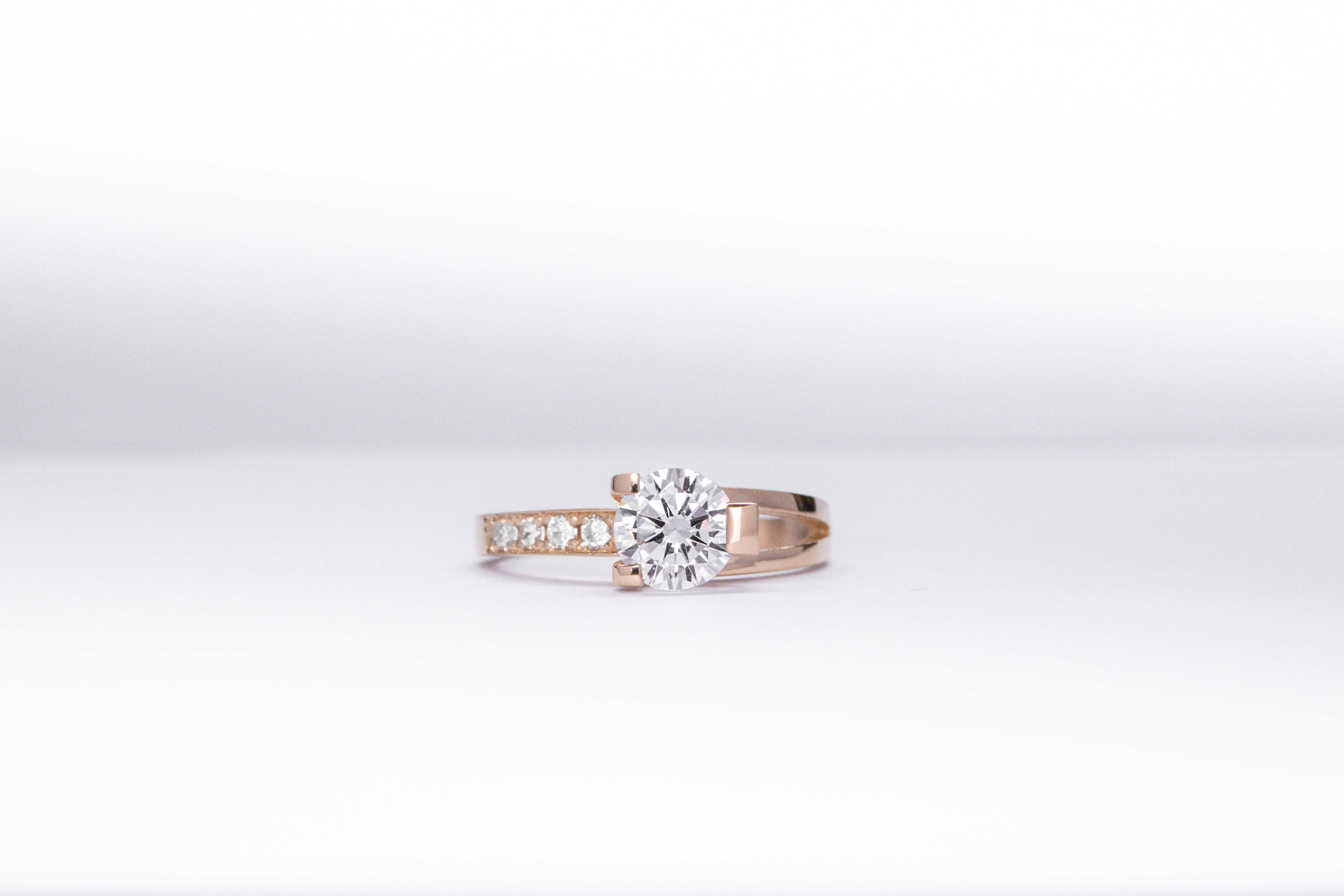 anillo de compromiso de oro 18k rosa con un diamante central y 4 diamantes mas pequeños en el costado sobre fondo blanco
