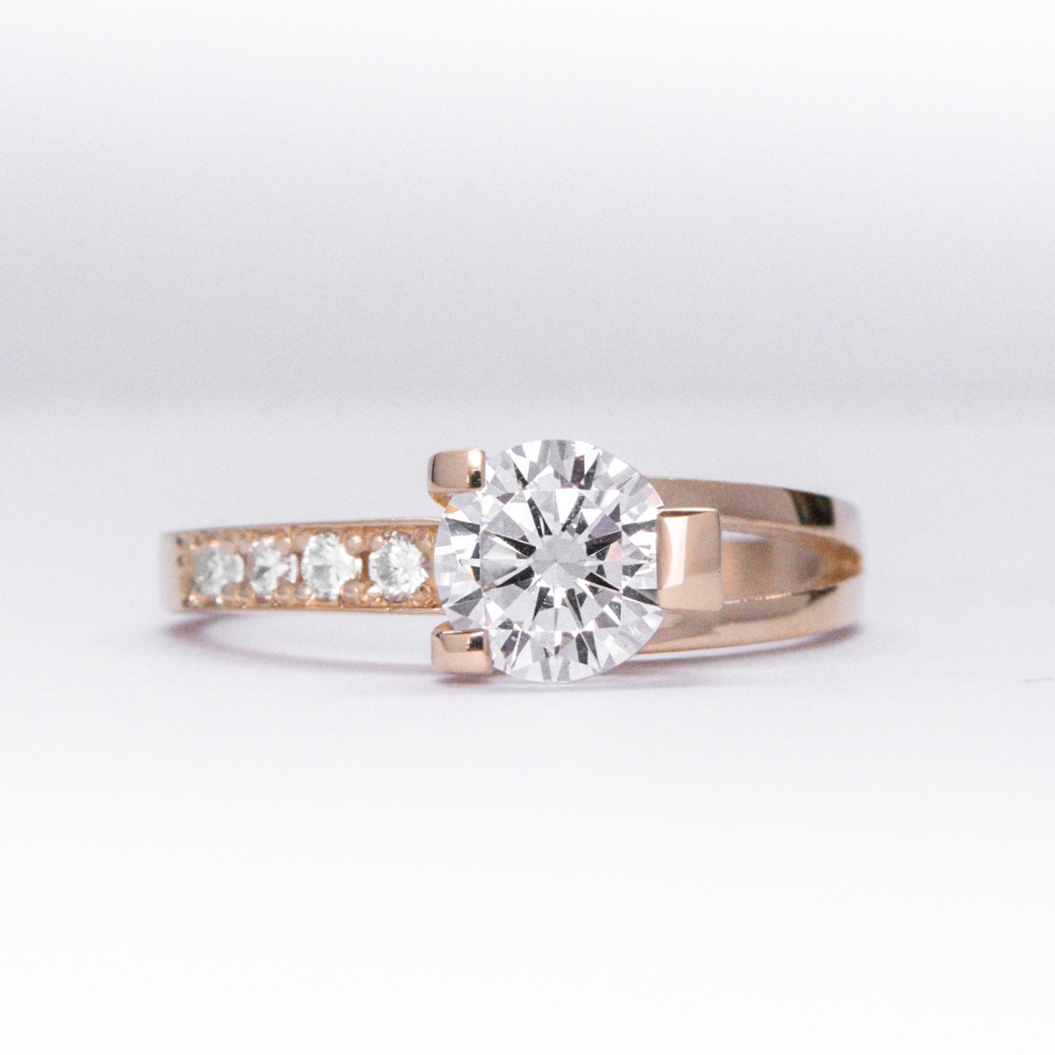anillo de compromiso de oro 18k rosa con un diamante central y 4 diamantes mas pequeños en el costado sobre fondo blanco