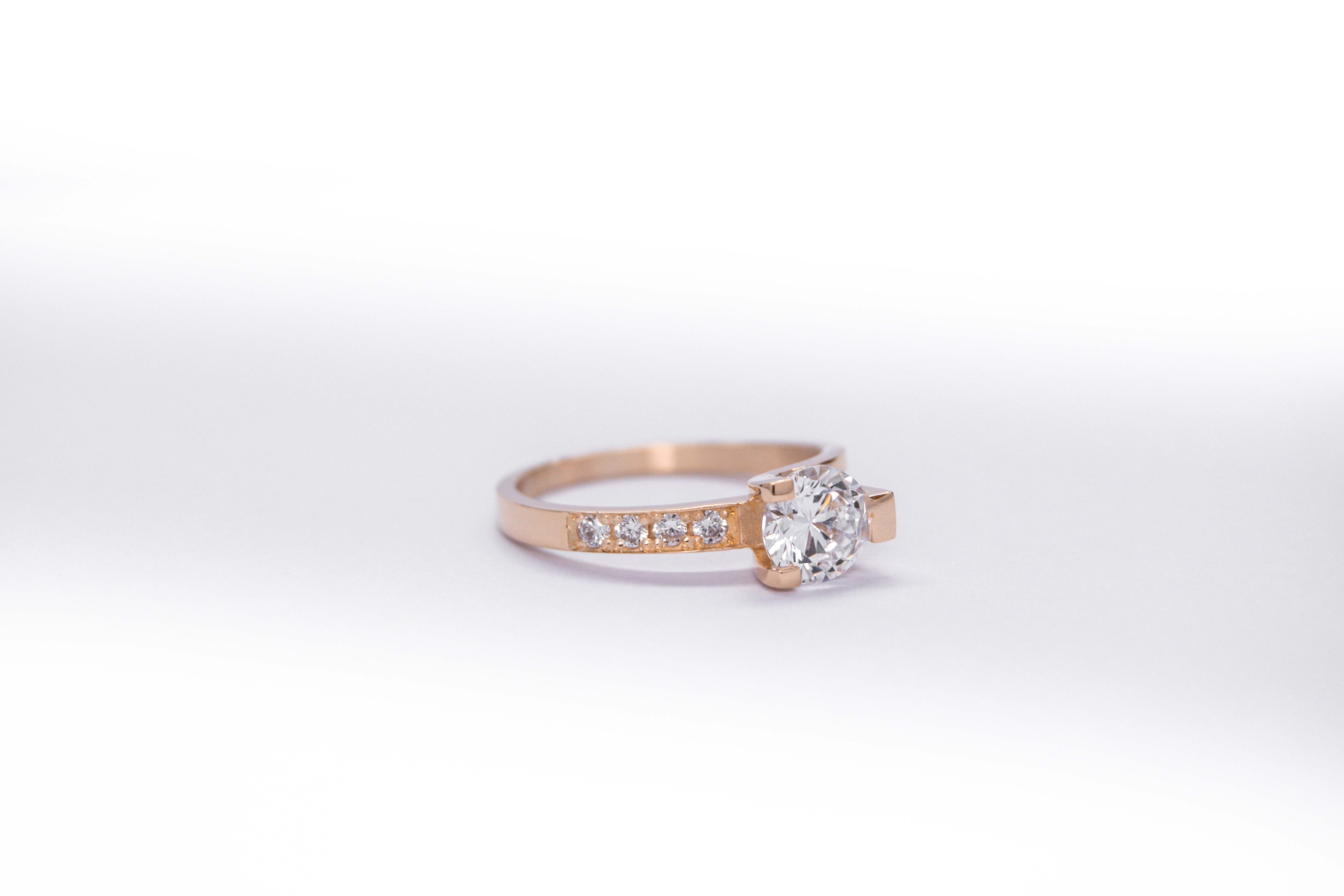 anillo de compromiso de oro 18k rosa con un diamante central y 4 diamantes mas pequeños en el costado sobre fondo blanco