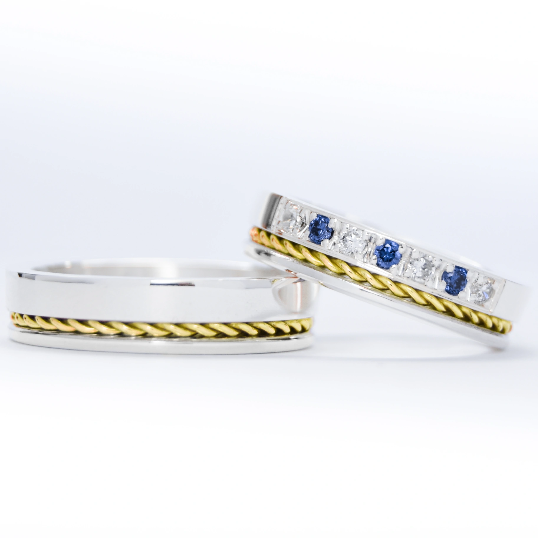 Alianzas de plata 950k y oro 18k amarillo con diamantes blancos y zafiros engarzadas. sobre fondo blanco.