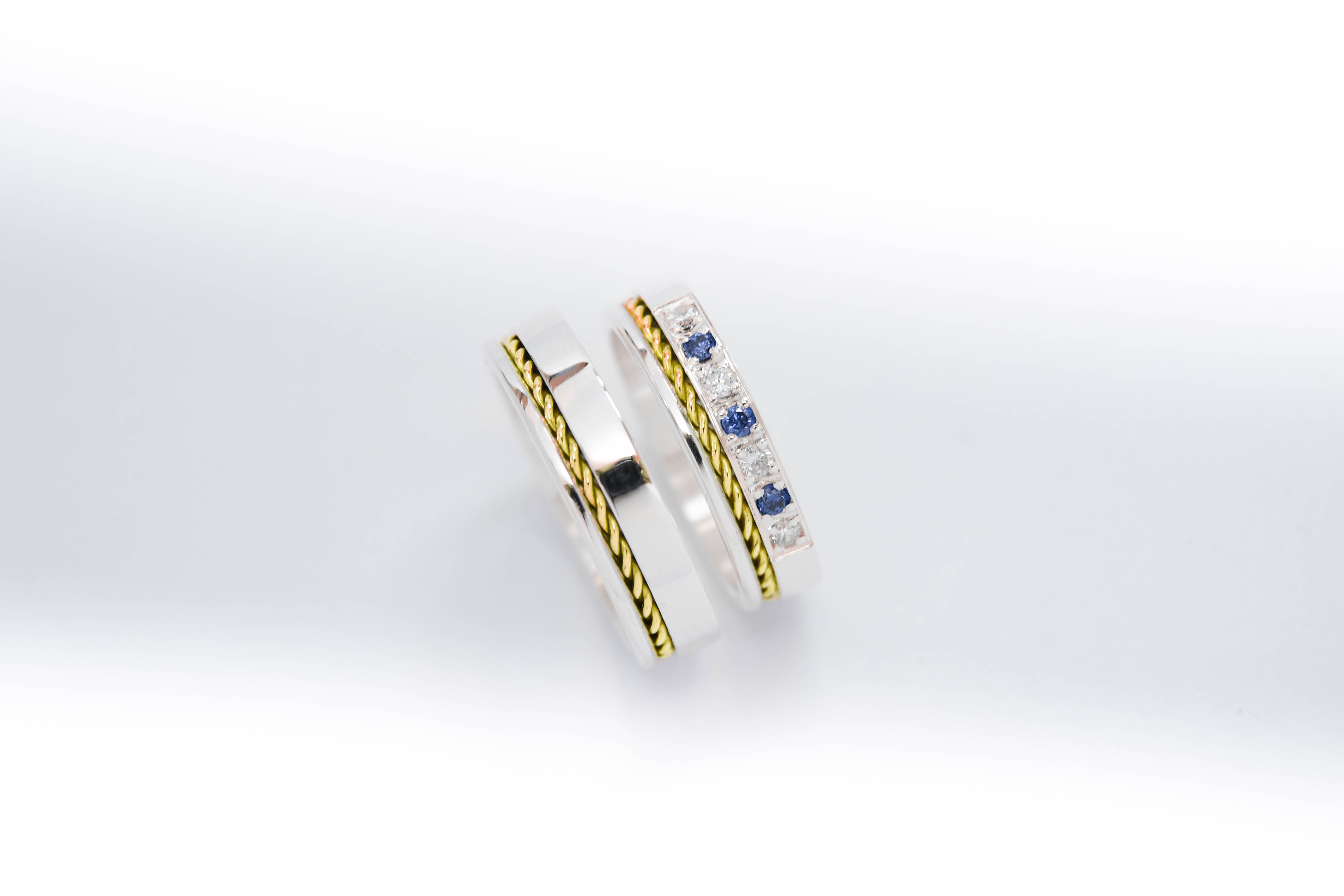 Alianzas de plata 950k y oro 18k amarillo con diamantes blancos y zafiros engarzadas. sobre fondo blanco.
