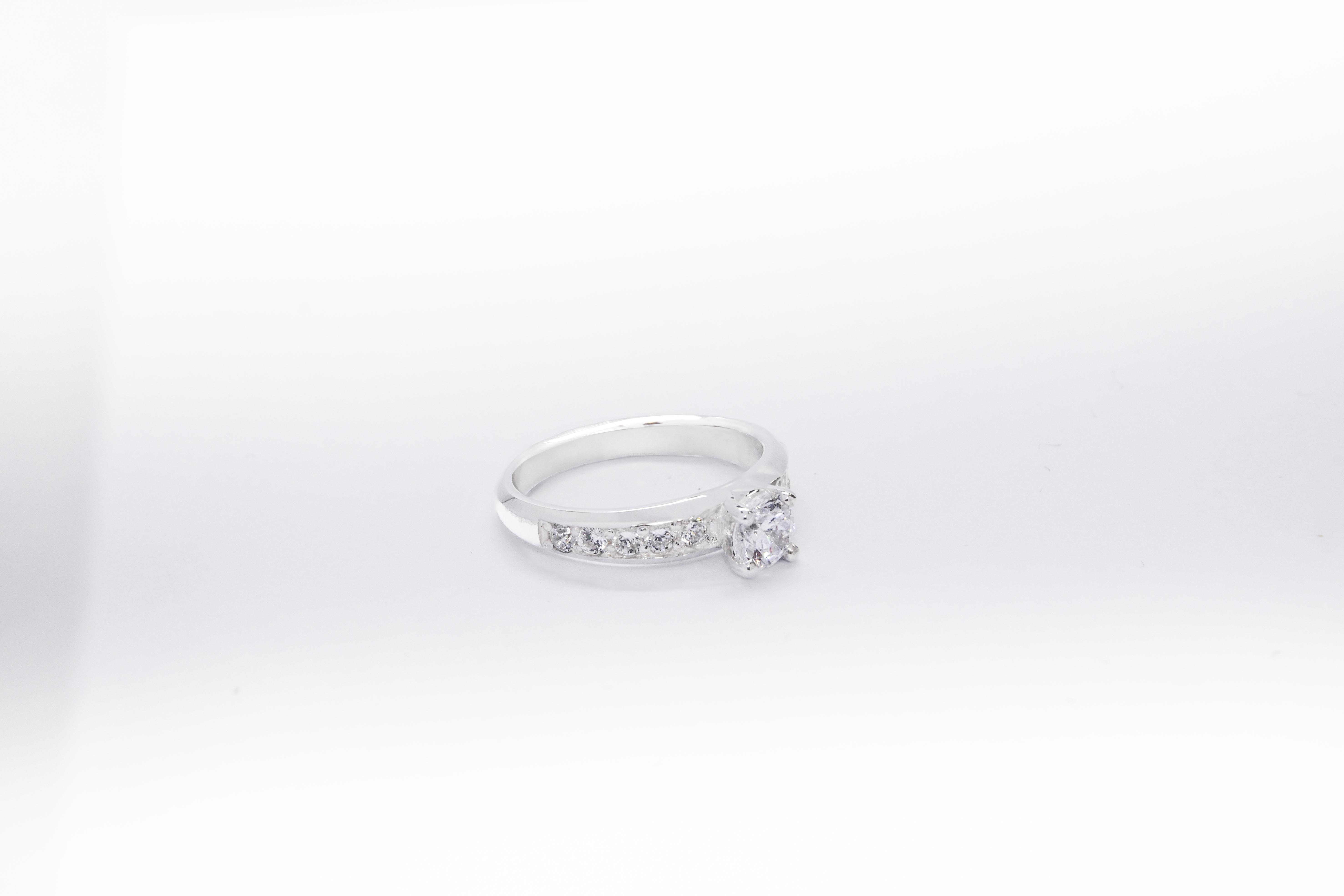 Anillo de compromiso de plata 925k con una gema blanca brillante y otras a los costados sobre fondo blanco