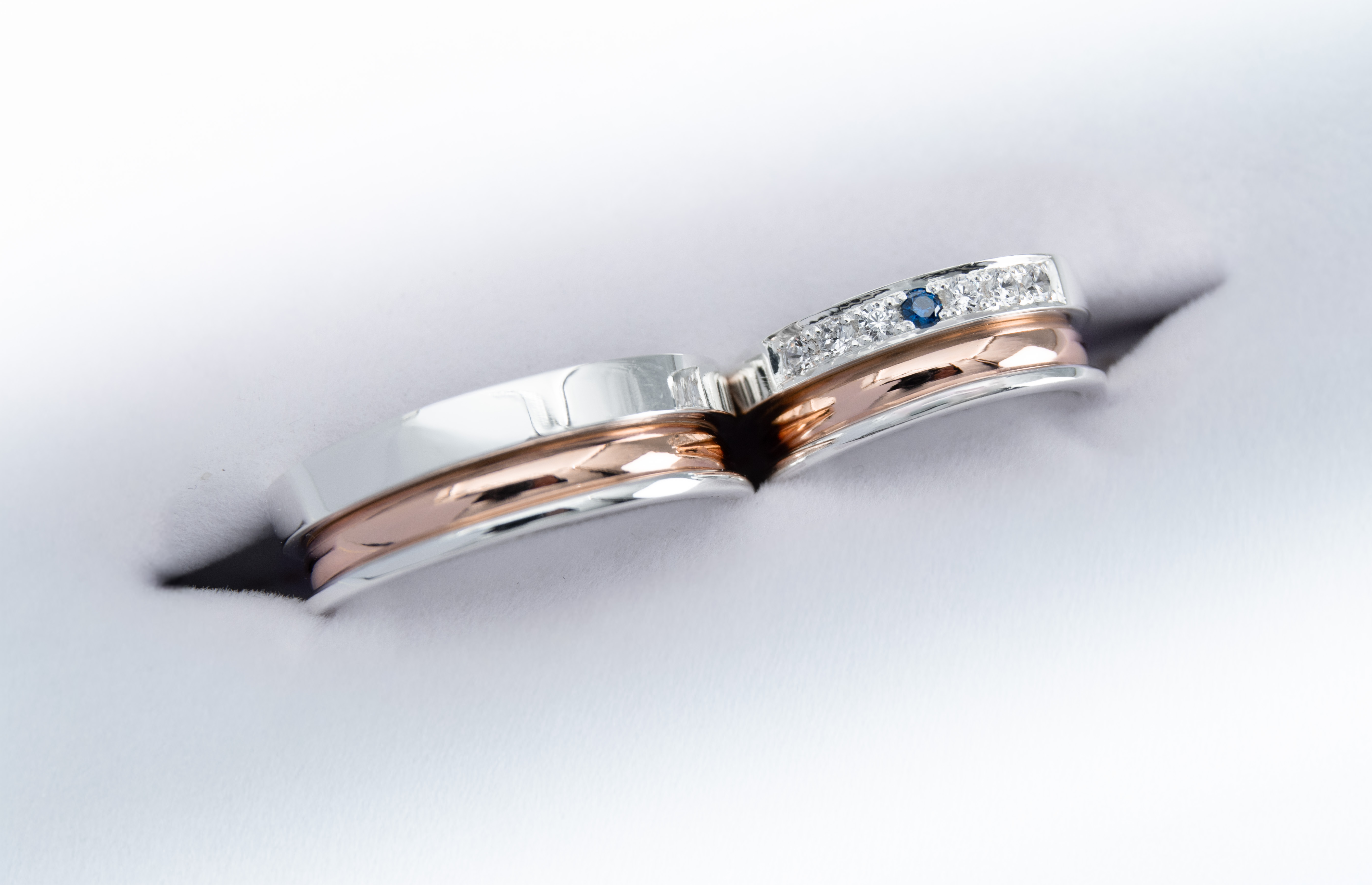un par de alianzas de plata y oro 18k Rosa con gemas engarzadas en el anillo de la mujer blancas y azul zafiro sobre fondo blanco