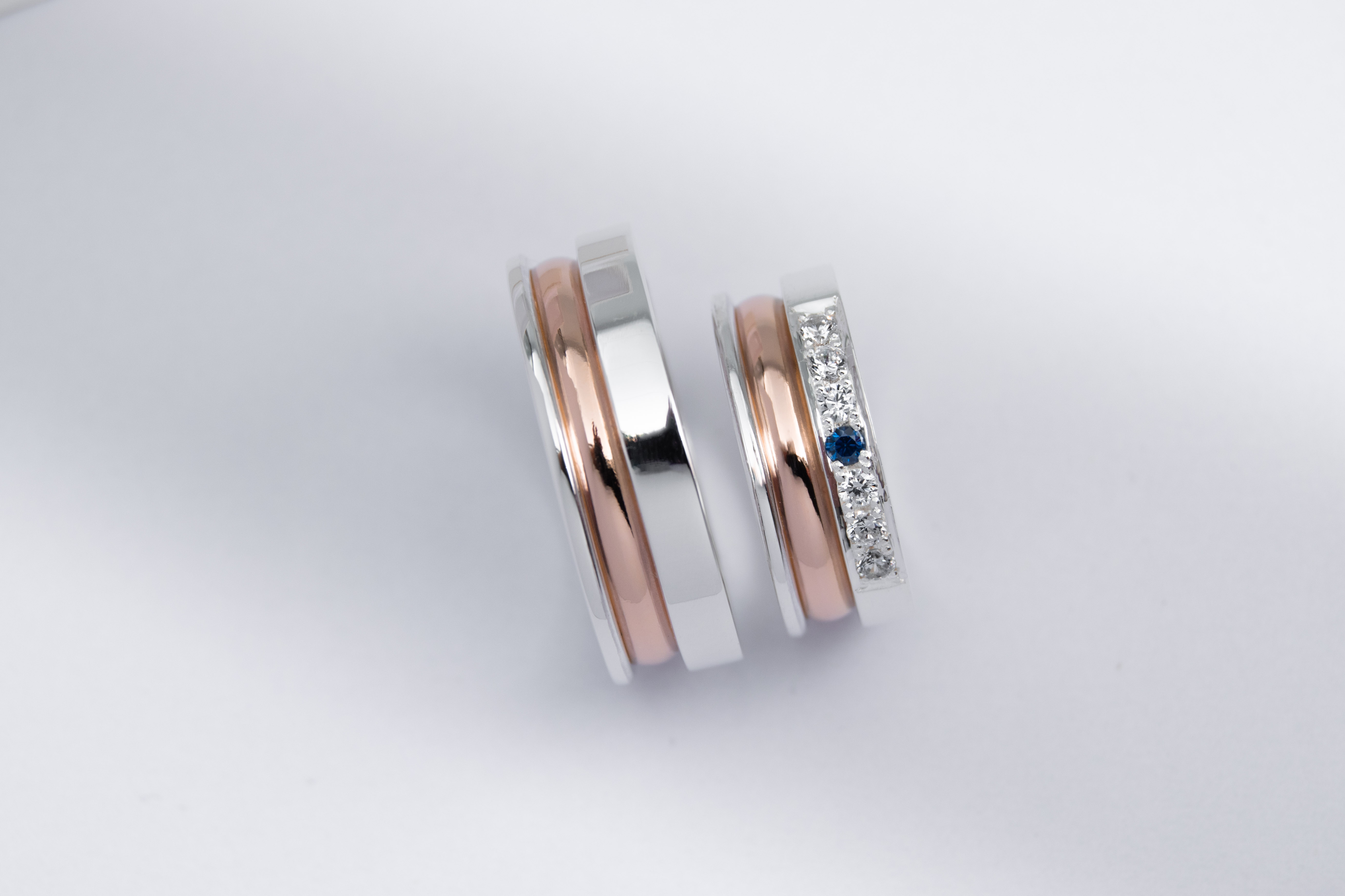 un par de alianzas de plata y oro 18k Rosa con gemas engarzadas en el anillo de la mujer blancas y azul zafiro sobre fondo blanco