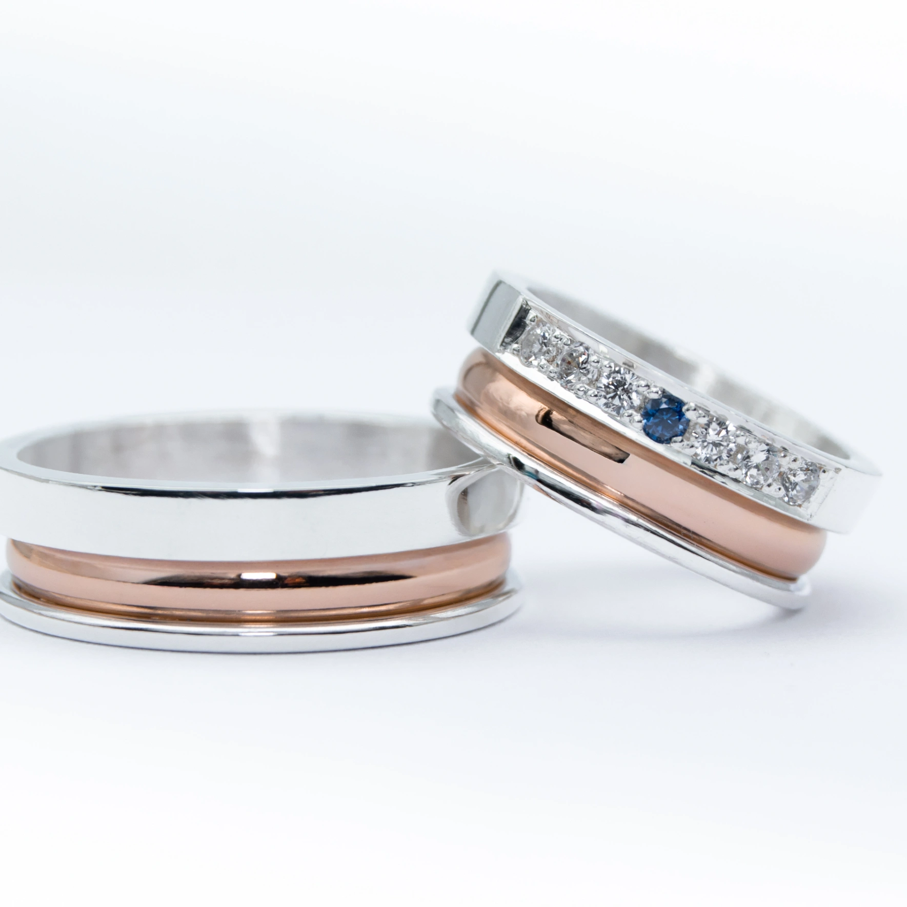 un par de alianzas de plata y oro 18k Rosa con gemas engarzadas en el anillo de la mujer blancas y azul zafiro sobre fondo blanco