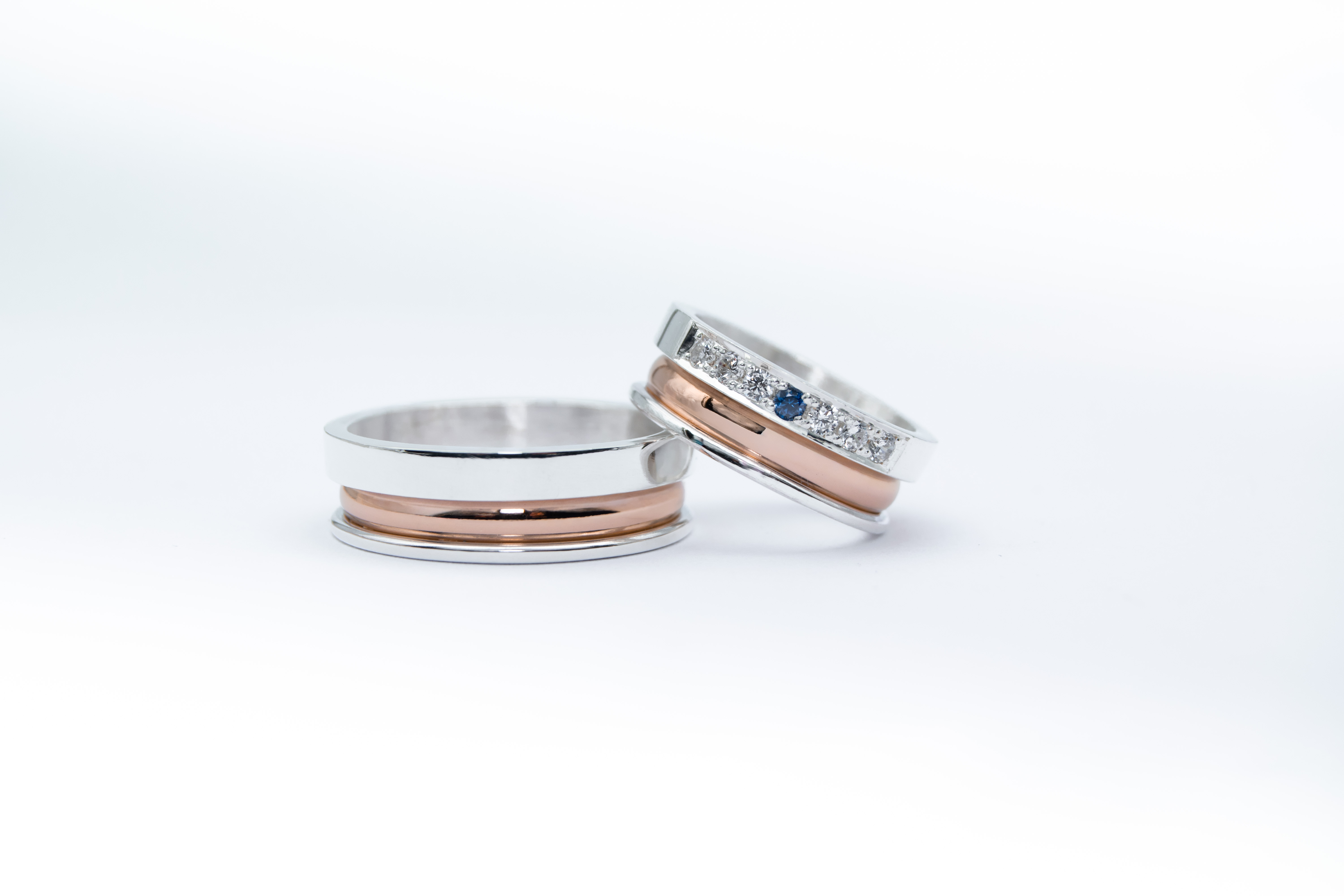 un par de alianzas de plata y oro 18k Rosa con gemas engarzadas en el anillo de la mujer blancas y azul zafiro sobre fondo blanco