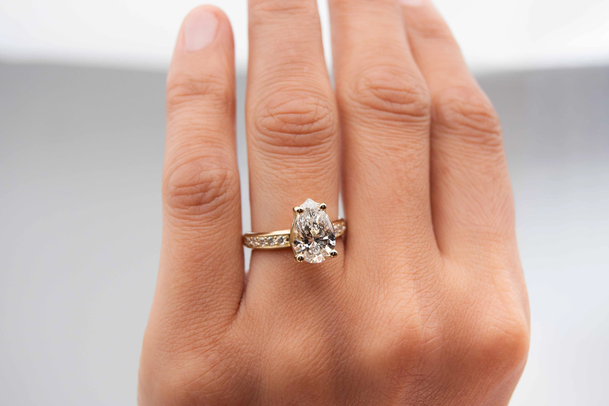 anillo de compromiso de oro modelo Taylor más con gema pear cut en la mano de la modelo